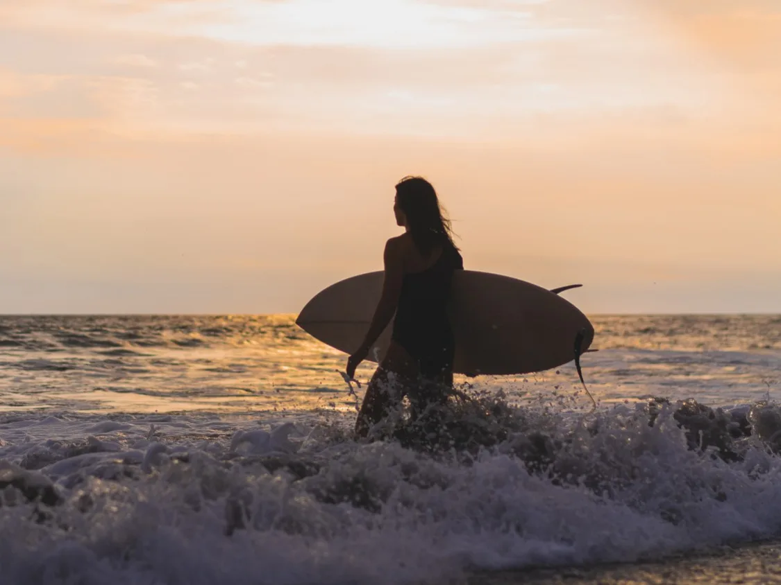 Surfista entrando al mar con su tabla al atardecer